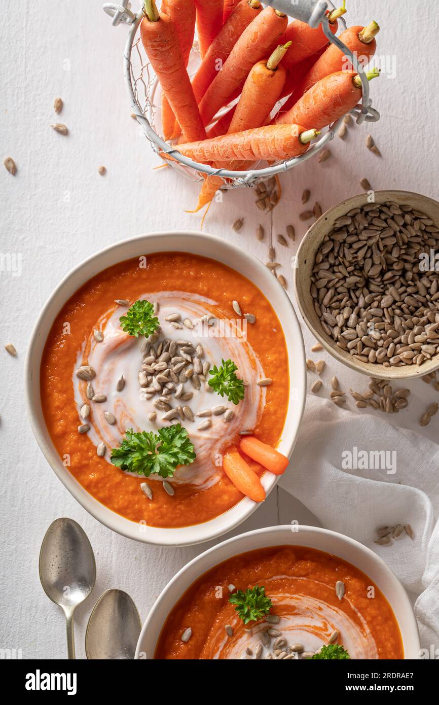 Rote Karottensuppe als saisonales Gericht. Karottensuppe mit Kräutern und Samen in einer weißen Schüssel. Stockfoto