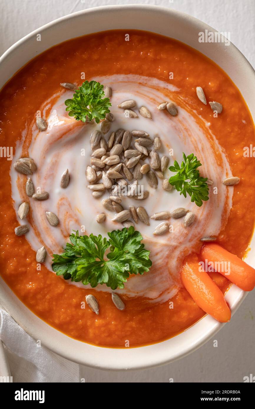 Vegane Karottensuppe als saisonales Gericht. Karottensuppe mit Kräutern und Samen in einer weißen Schüssel. Stockfoto