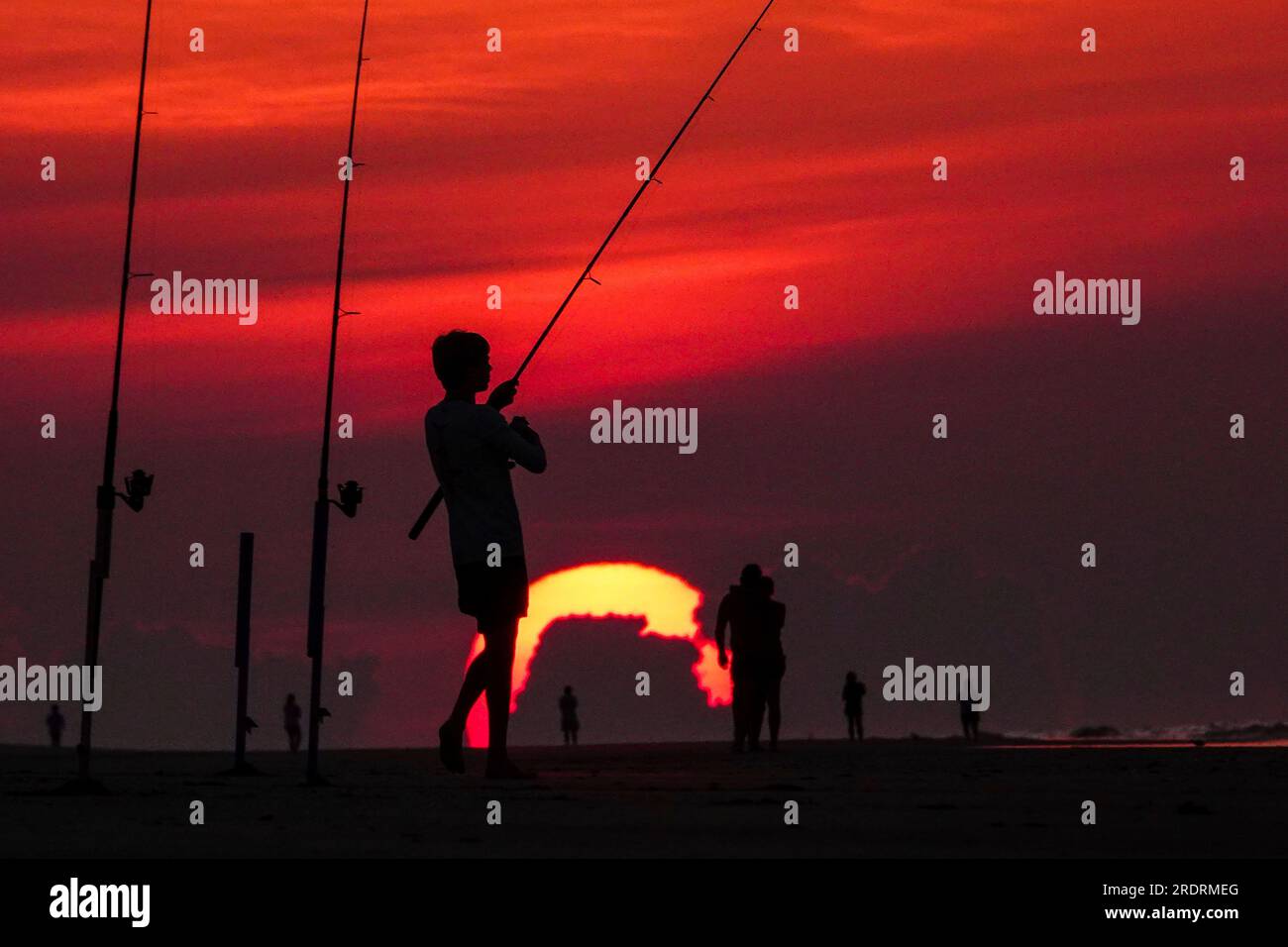 Isle Of Palms, Usa. 23. Juli 2023. Ein Fischer, der vor einem dramatischen Sonnenaufgang als Riesenball über dem Strand auftaucht, am 23. Juli 2023 auf der Isle of Palms, South Carolina. Eine anhaltende Hitzewelle über den Süden der USA bringt weiterhin extrem heißes, feuchtes Wetter in die Region. Kredit: Richard Ellis/Richard Ellis/Alamy Live News Stockfoto