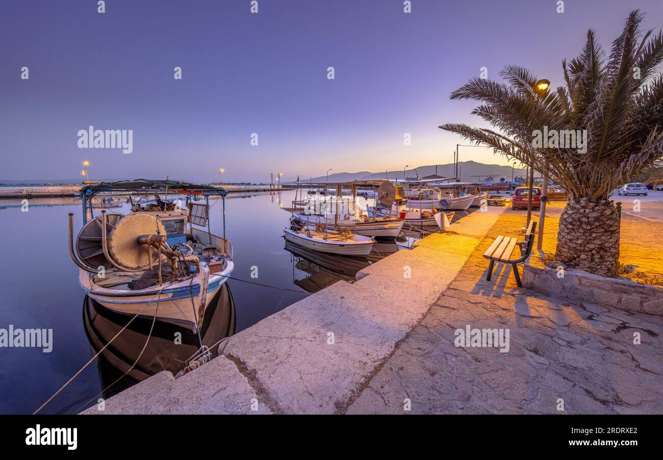 Fischerhafen-Szene in Griechenland mit Booten, Palmen und Motorrollern bei Nacht an einem wunderschönen ruhigen Sommertag Stockfoto
