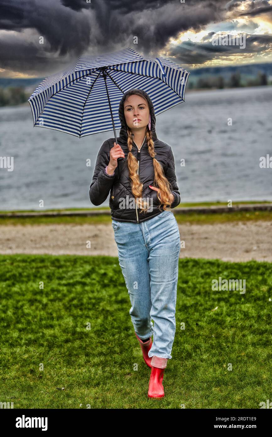 Junge Frau mit Schirm am See auf einer grünen Wiese Stockfoto