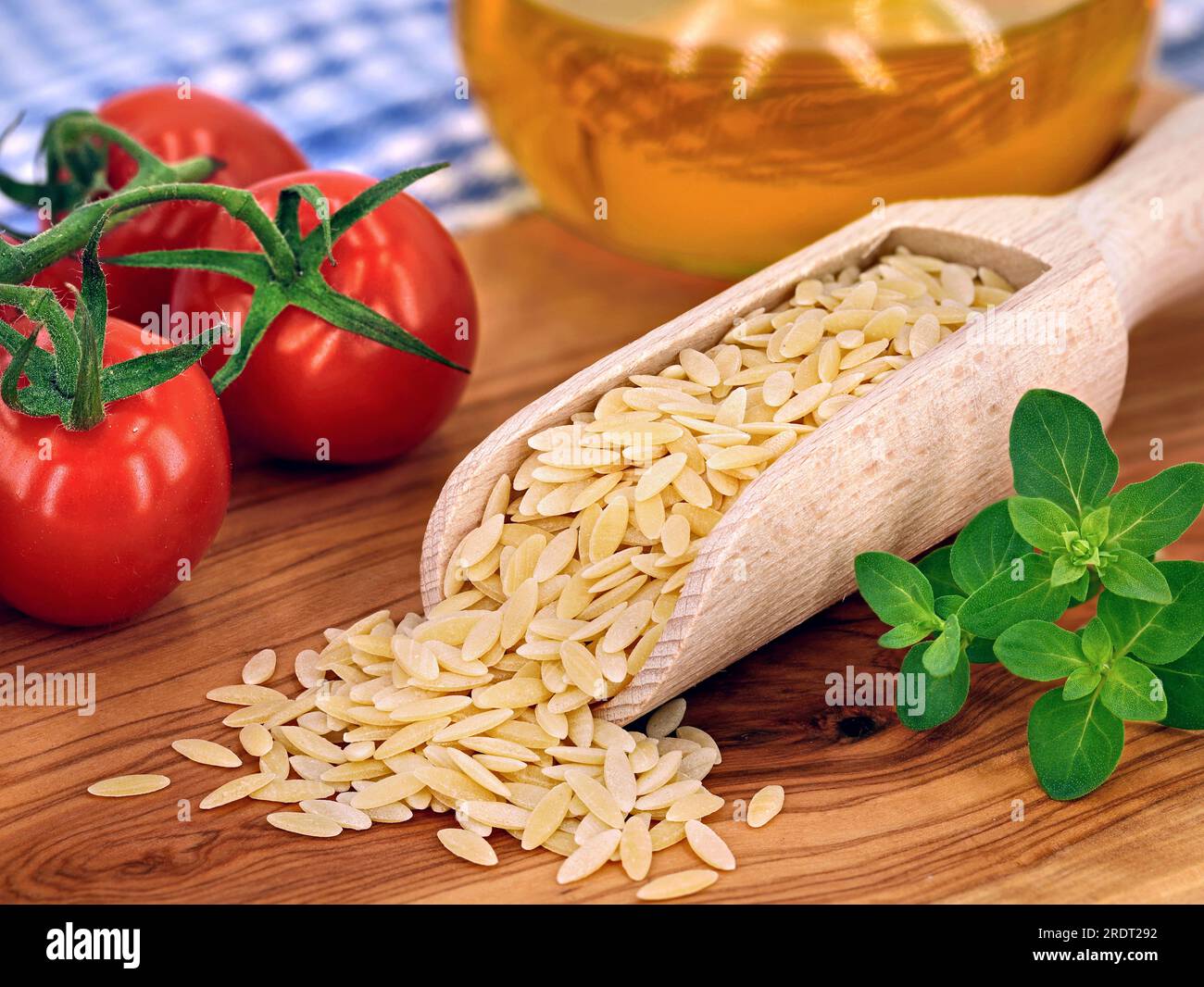 Nicht gekochte griechische Nudeln, Kritharaki in Holzlöffel auf Schneidebrett für Olivenholz mit frischen Tomaten und Oregano Stockfoto