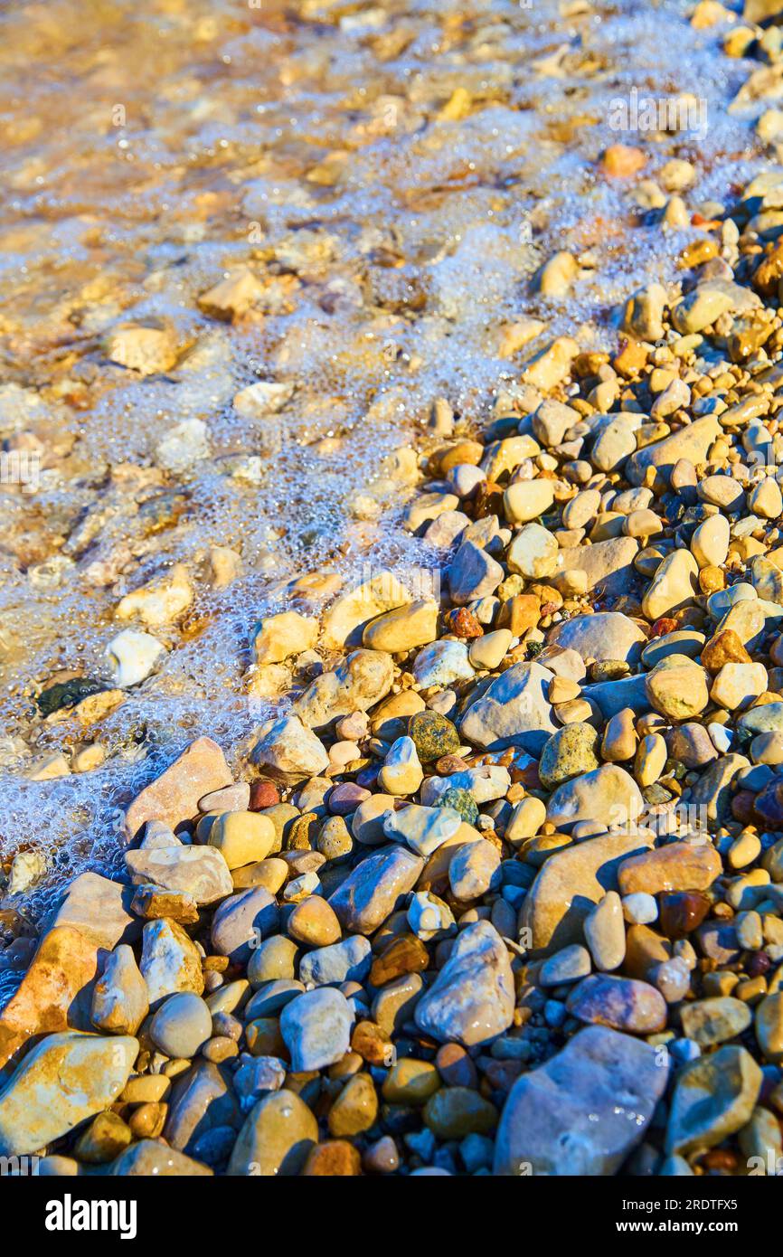 Wasser fließt über kleine Felsen und Steine am Ufer eines Teichs oder Sees Stockfoto
