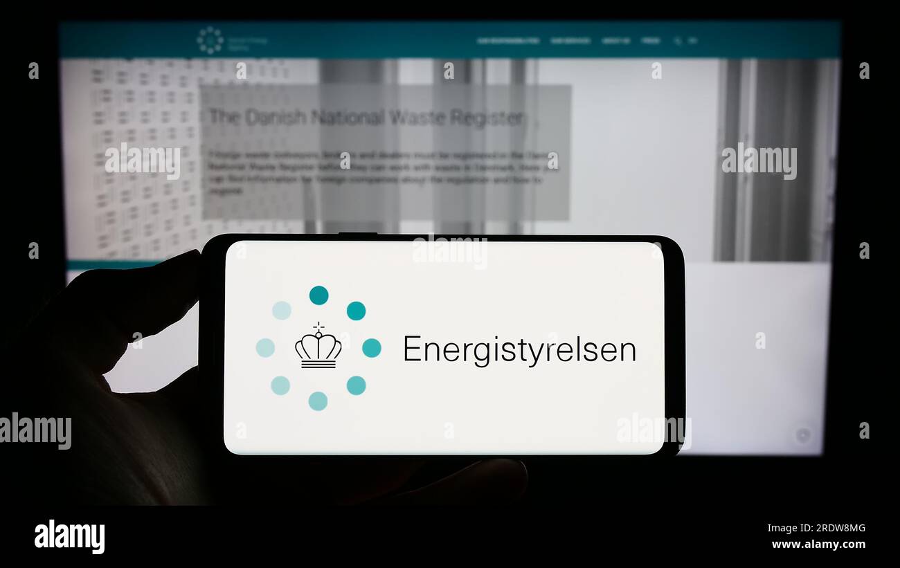 Person, die ein Mobiltelefon mit dem Logo der dänischen Energieagentur Energistyrelsen auf dem Bildschirm vor der Webseite hält. Konzentrieren Sie sich auf das Display des Telefons. Stockfoto