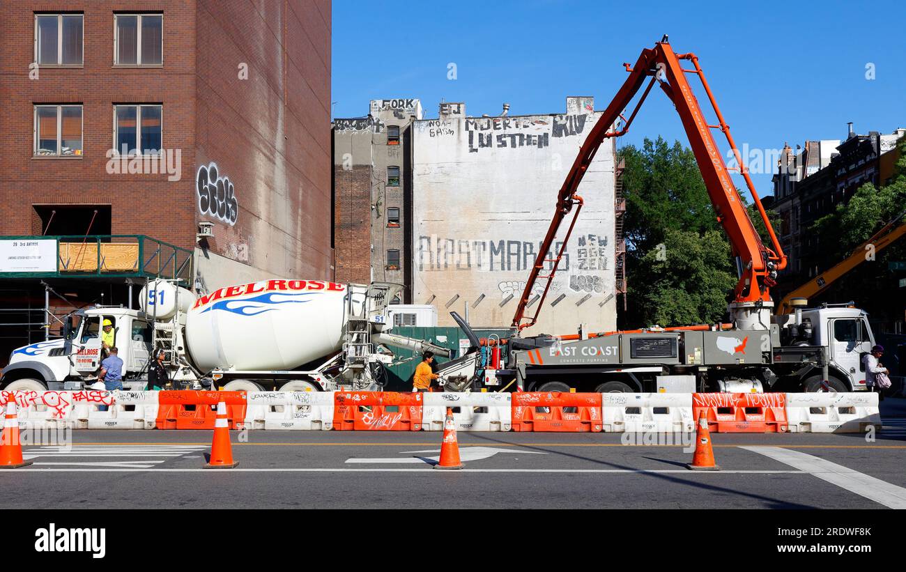 Ein Betonpumpenwagen und ein Betonmischwagen auf einer Baustelle in New York City. Der Pumpenwagen hat einen ausfahrbaren Ausleger für die Reichweite. Stockfoto