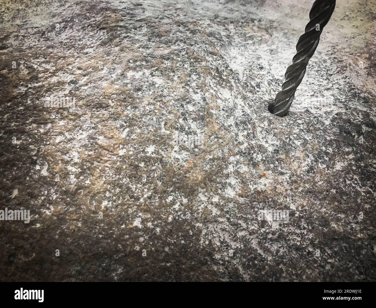 Ein robuster Hartmetallbohrer bohrt ein Loch in einen großen grauen Stein. Ansicht schließen. Der Hintergrund. Stockfoto