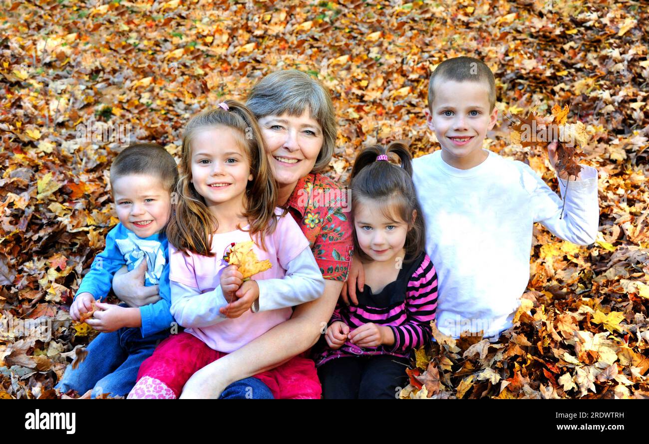 Laub harken und Spaß haben ist die Tradition dieser Familie. Großmutter hat zwei ihrer Enkelkinder und die anderen zwei sitzen neben ihr. Sie sind faul Stockfoto