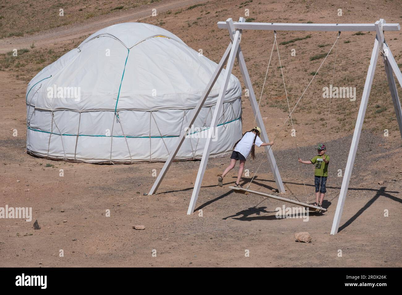 Kasachstan, Charyn Canyon. Kinder spielen auf einer Schaukel, Jurt im Hintergrund. Stockfoto