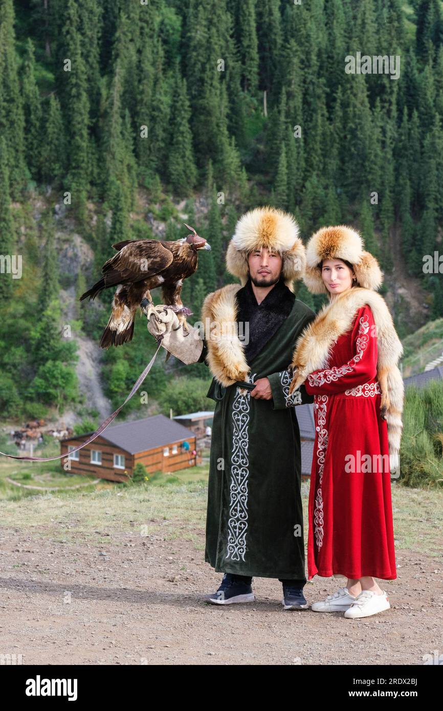 Kasachstan, Kolsay-Seen-Nationalpark. Ein Paar posiert für ein Foto in traditionellem Kostüm mit Falke mit Kapuze. Stockfoto