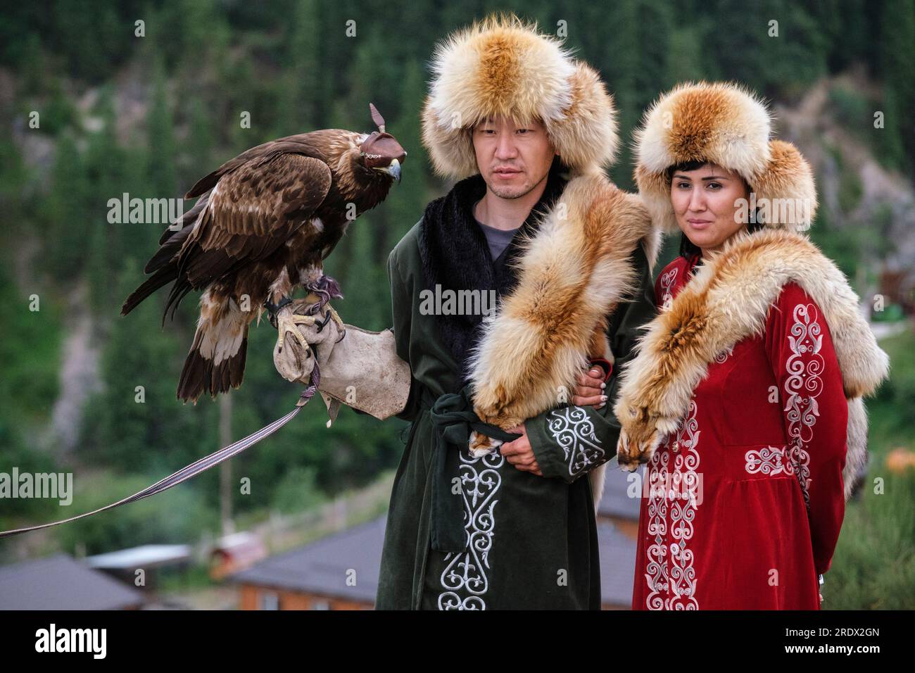 Kasachstan, Kolsay-Seen-Nationalpark. Ein Paar posiert für ein Foto in traditionellem Kostüm mit Falke mit Kapuze. Stockfoto