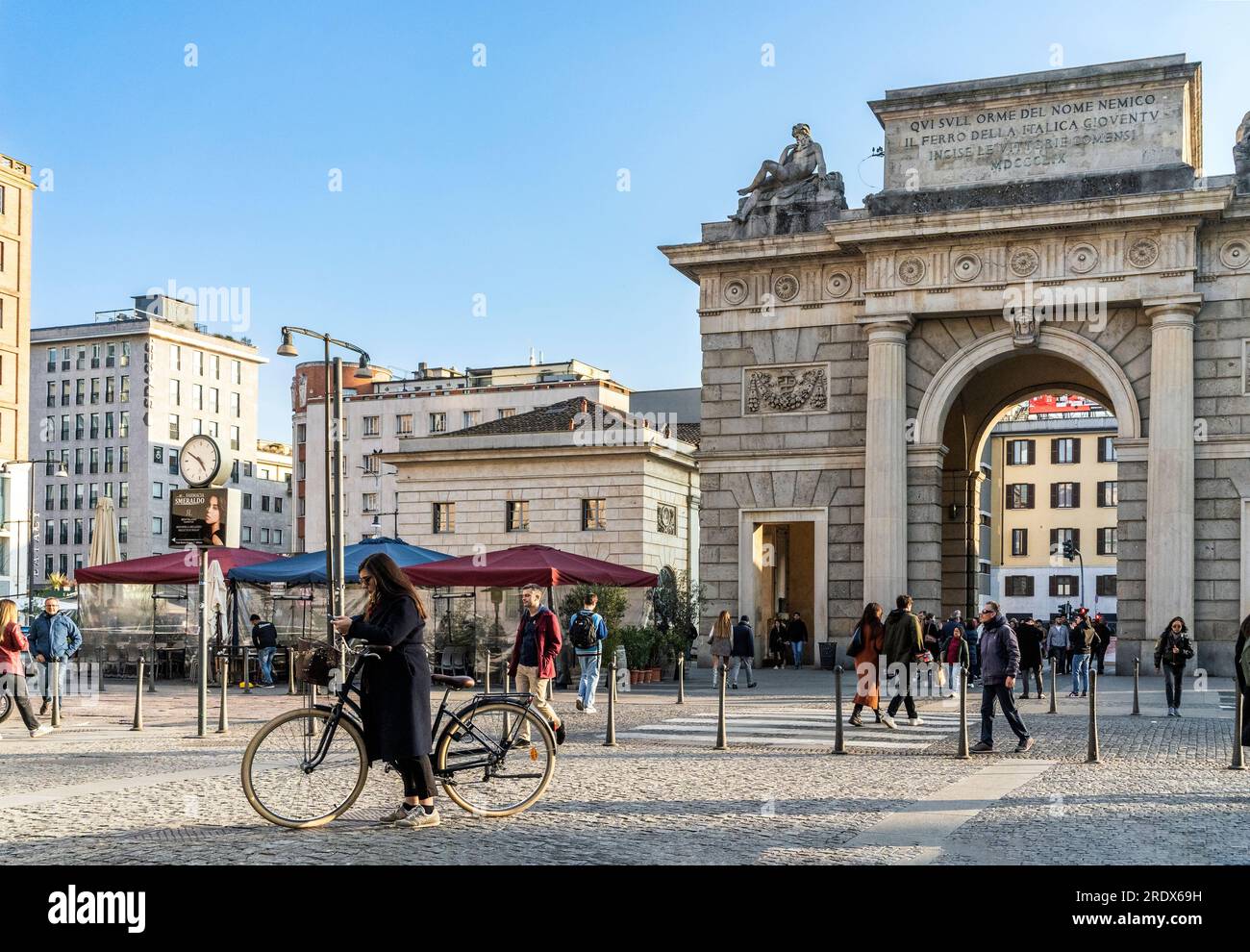 Piazza XXV Aprile with people walking and a cyclist. In the background, Porta Garibaldi gate. Milan city center, Lombardy region, Italy Stockfoto