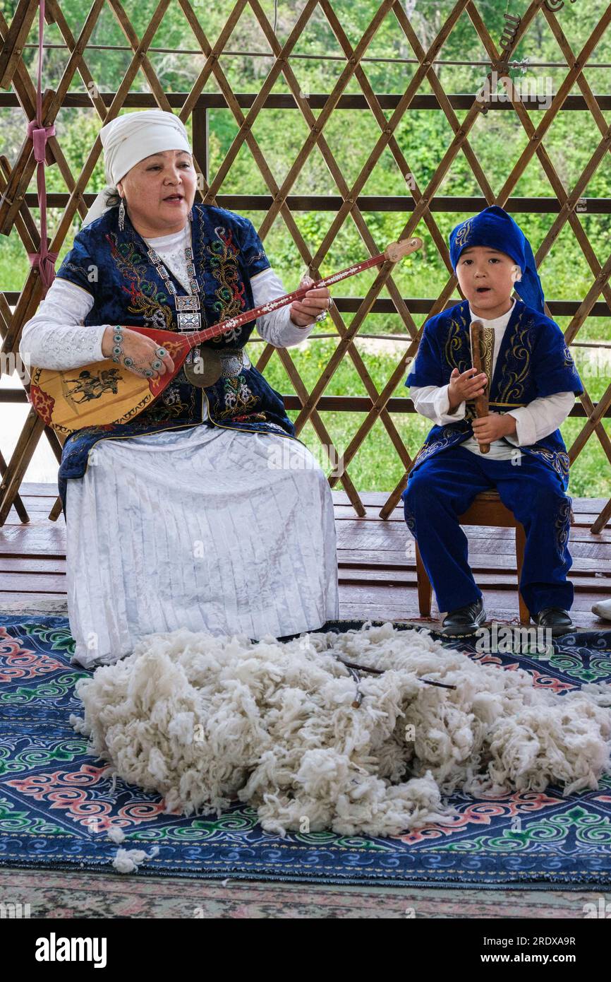 Kasachstan, Hunnen-Ethno-Dorf. Eine Kasacherin mittleren Alters, die Dombra spielt. Wolle auf dem Boden. Stockfoto