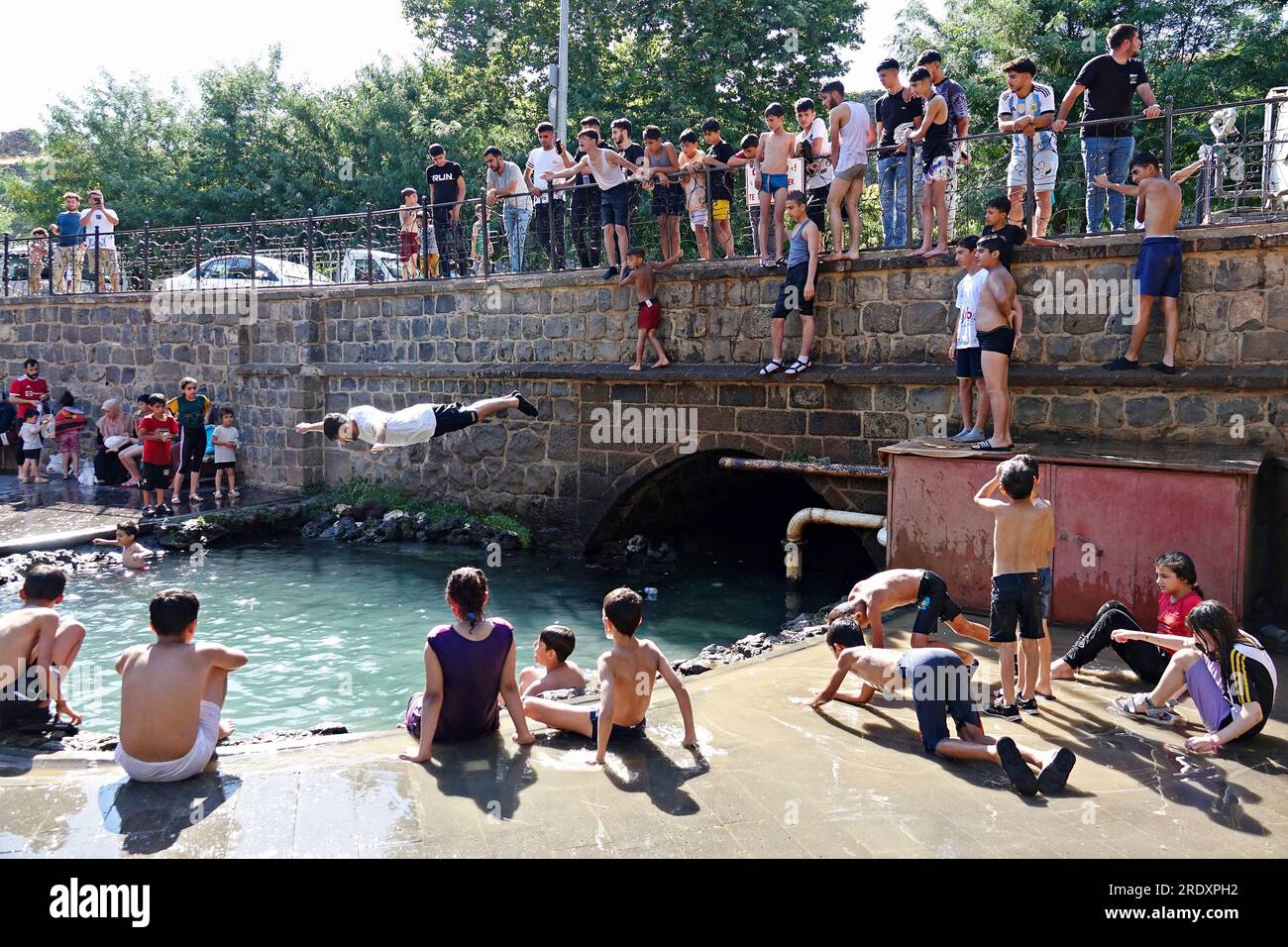 Ein hitzebefallener Teenager springt aus einer Höhe in den historischen Grundwasserpool Anzele in Diyarbakir, eine der heißesten Städte der Türkei, im Südosten der Türkei. Die extreme Hitzewelle aus Nordafrika hat die gesamte Türkei getroffen. Die Wetterbehörden gaben eine Hitzewarnung für 40 Provinzen aus. In den meisten Teilen der Türkei liegt die Lufttemperatur 5-10 Grad über den saisonalen Normen. Die Temperatur, die 40 Grad im Schatten erreicht, liegt bei etwa 50 Grad in der Sonne. Während die Strände voll sind in Städten mit Meeresstränden, versuchen die Leute sich abzukühlen, indem sie die W betreten Stockfoto