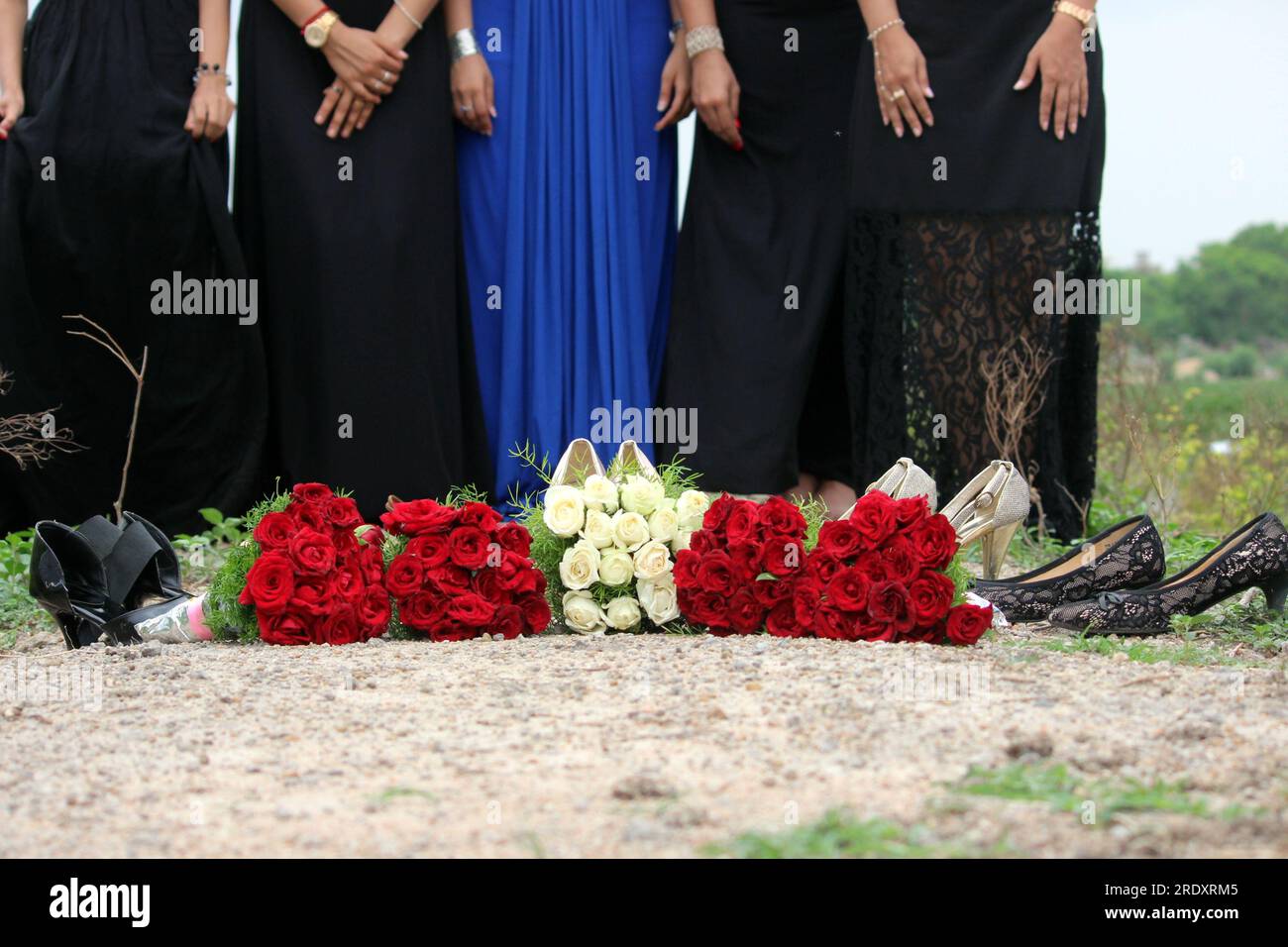 Brautjungfer-Konzept mit rot-weißen Rosen. Braut in Blau und andere Mädchen in schwarzem Kleid. Hochzeitsthema Fotohintergrund oder Miniaturbild. Stockfoto