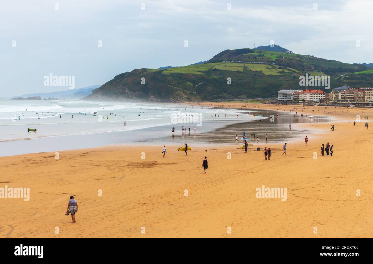 Spaziergänge am breiten Strand der Biscayne Bay, Spanien. Surfstrand mit Surfern und Berg im Hintergrund. Aktives Lifestyle-Konzept. Stockfoto