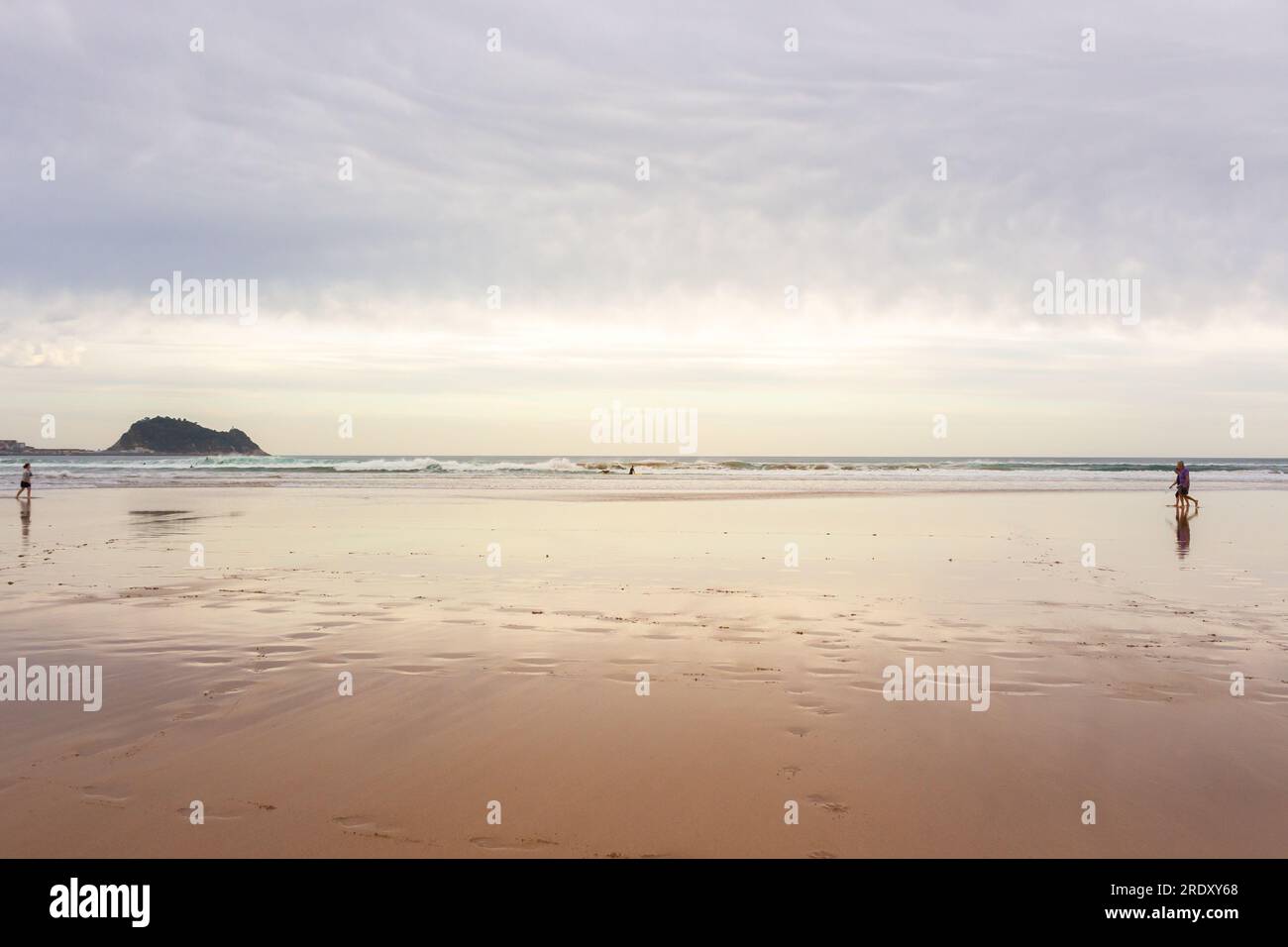 Spaziergänge am breiten Strand der Biscayne Bay, Spanien. Surfstrand mit Leuten. Aktives Lifestyle-Konzept. Unbekannte Leute, die am Strand spazieren gehen. Stockfoto