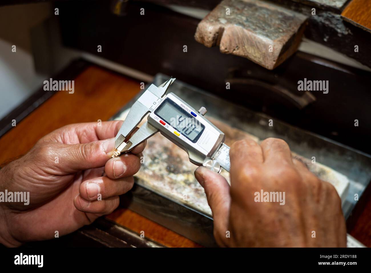 Juwelierhände messen und prüfen die Größe goldener Juwelen mit einem Messschieber. Goldschmied, der in seiner Schmuckwerkstatt arbeitet. Stockfoto