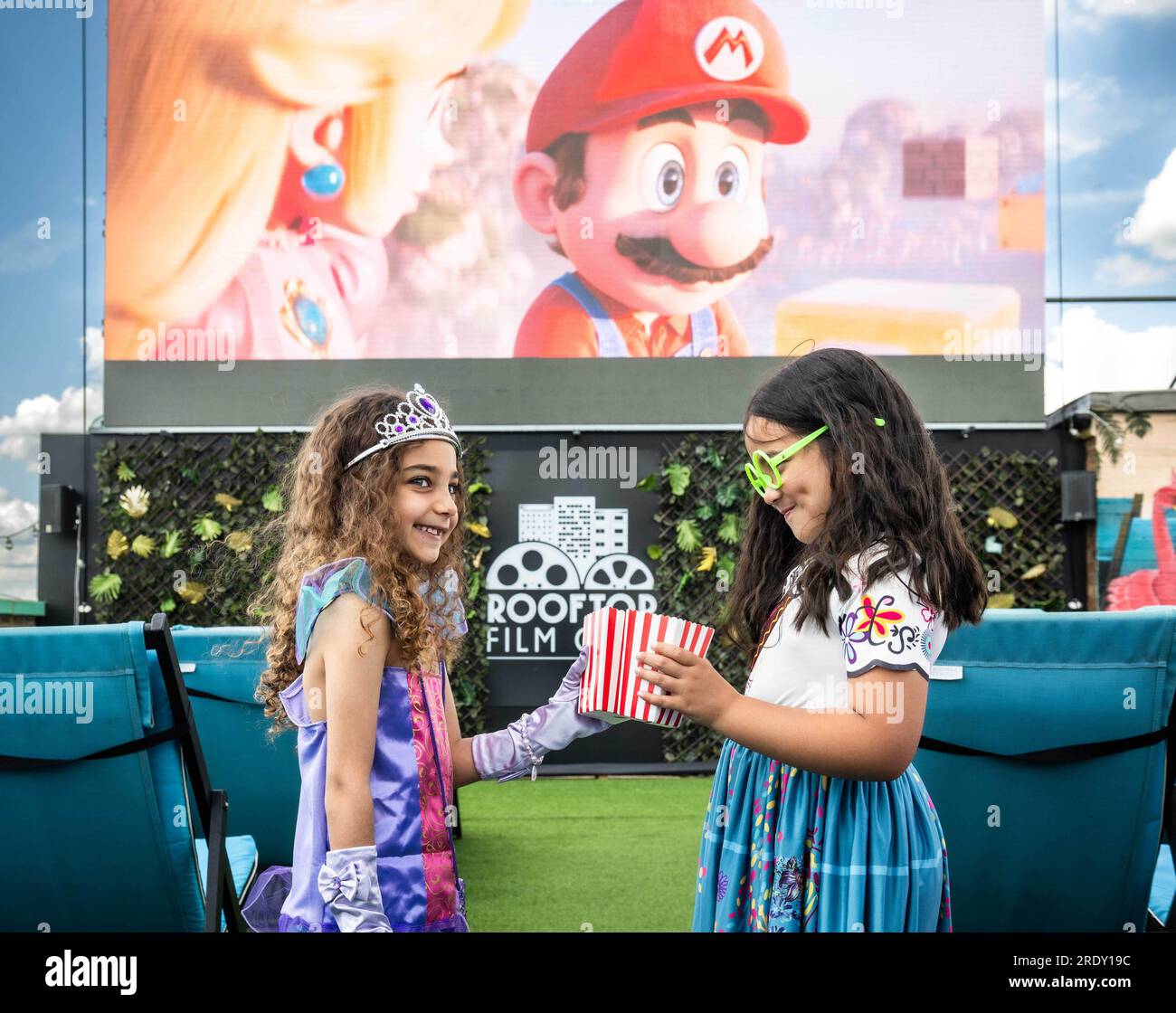 NUR REDAKTIONELLER GEBRAUCH (von links nach rechts) Kaylee Maya Kamand, 6, und Freyja Elizabeth Newman, 6, nehmen ihre Plätze bei einer Sommervorstellung der Super Mario Bros. Ein Film im Rooftop Film Club, Peckham. Ausgabedatum: Montag, 24. Juli 2023. Stockfoto