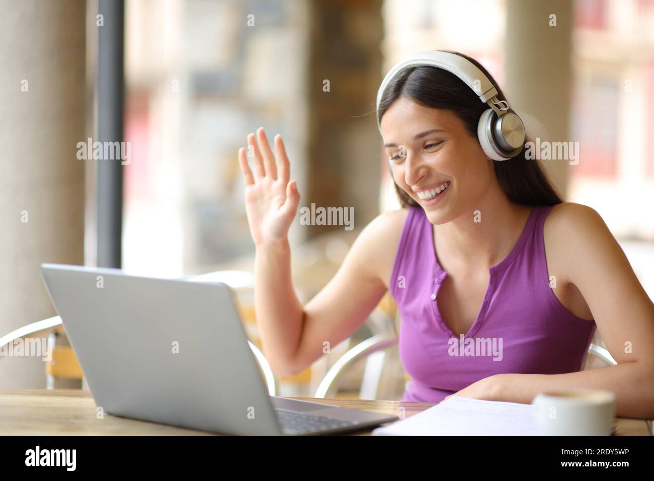 Glückliche Schülerin, die Video vall auf einem Laptop auf der Terrasse des Cafés hat Stockfoto