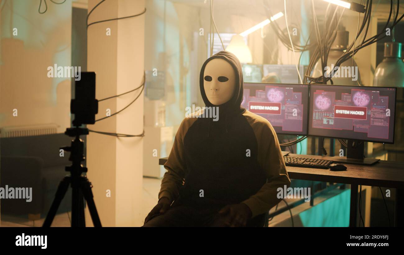 Männlicher Spion mit anonoym Maske, filmt Live-Bedrohungsvideo, fragt nach Ransomware, anstatt wichtige Daten zu verbreiten. Junge Person droht, Informationen preiszugeben, Online-Cyberkriminalität. Stockfoto