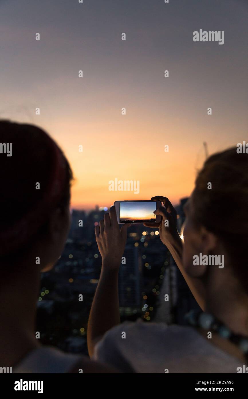 Freunde fotografieren Stadt mit orangefarbenem Himmel in der Dämmerung über ein Smartphone Stockfoto