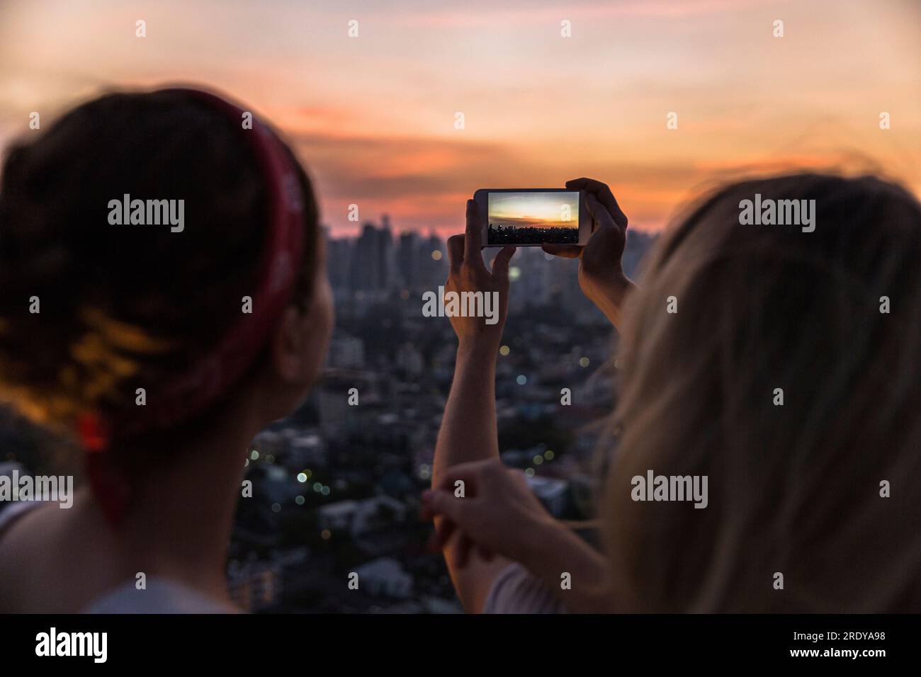Freunde, die in der Abenddämmerung mit dem Smartphone den Blick auf die Stadt fotografieren Stockfoto