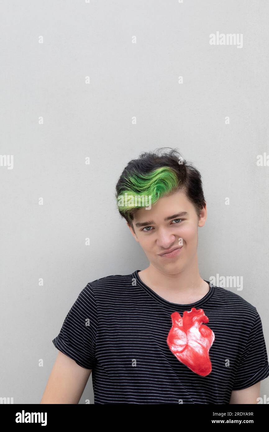 Teenager mit gefärbtem grünen Haar und künstlichem Herz vor grauem Hintergrund Stockfoto