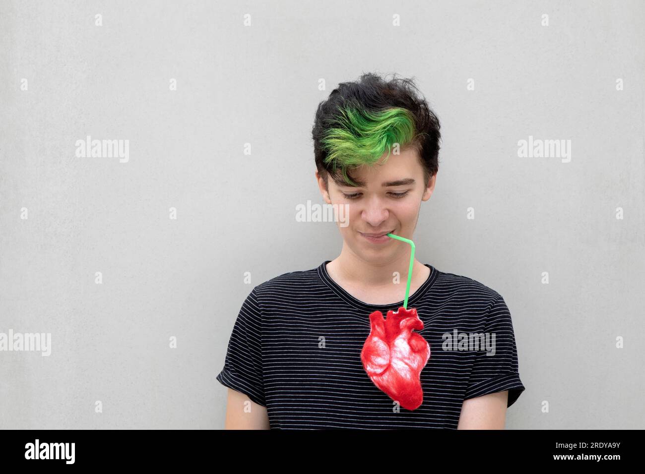 Ein Teenager mit grünem Haar trinkt aus dem Herzen vor grauem Hintergrund Stockfoto