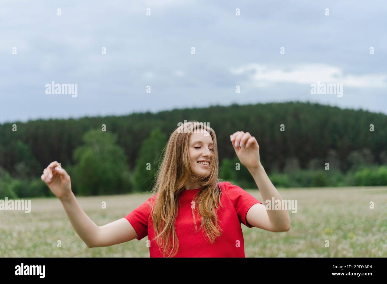 Lächelnde junge Frau in rotem T-Shirt, die auf dem Feld tanzt Stockfoto