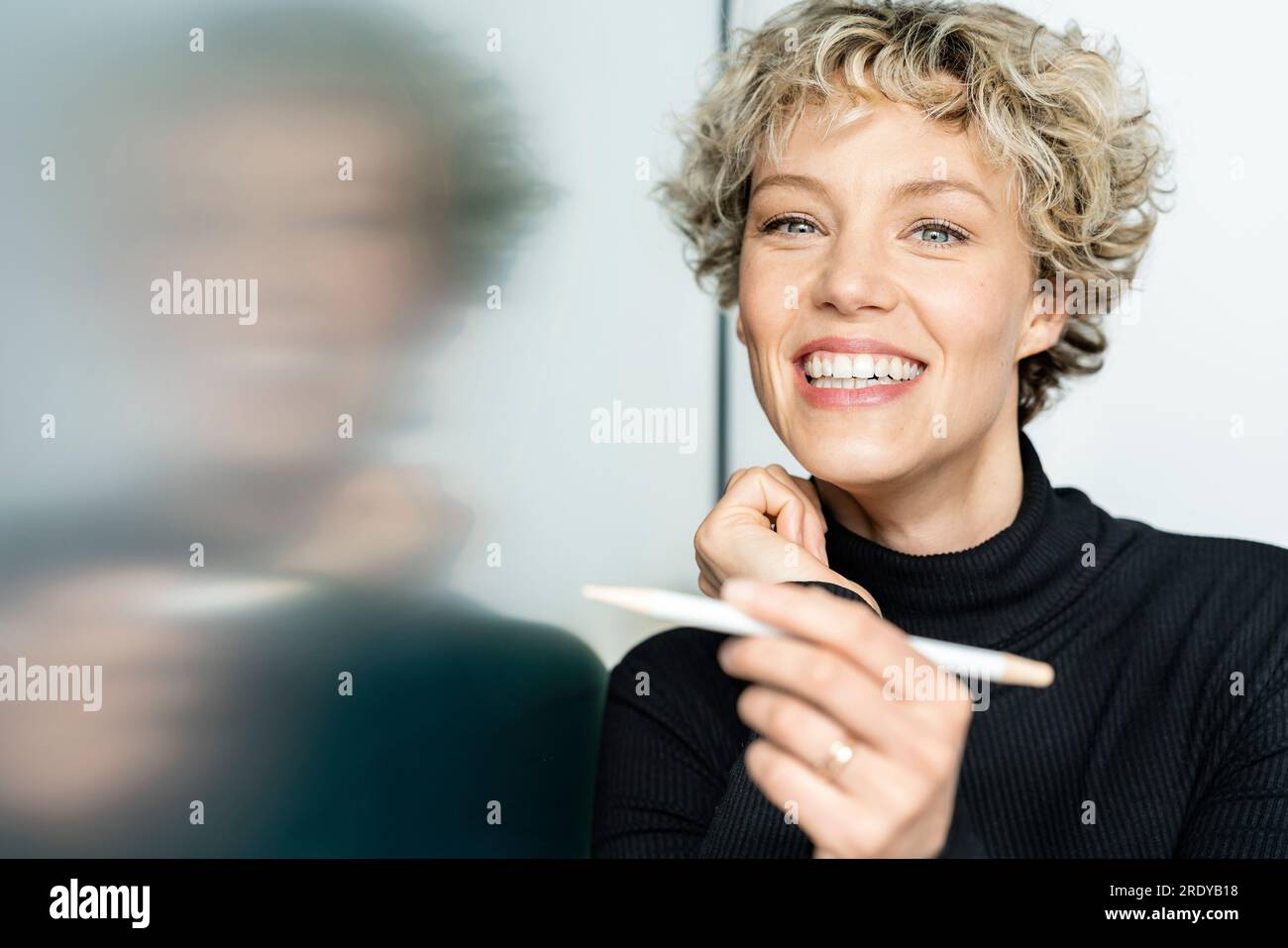 Glückliche Geschäftsfrau mit digitalisiertem Stift, der auf ein interaktives Whiteboard zeigt Stockfoto