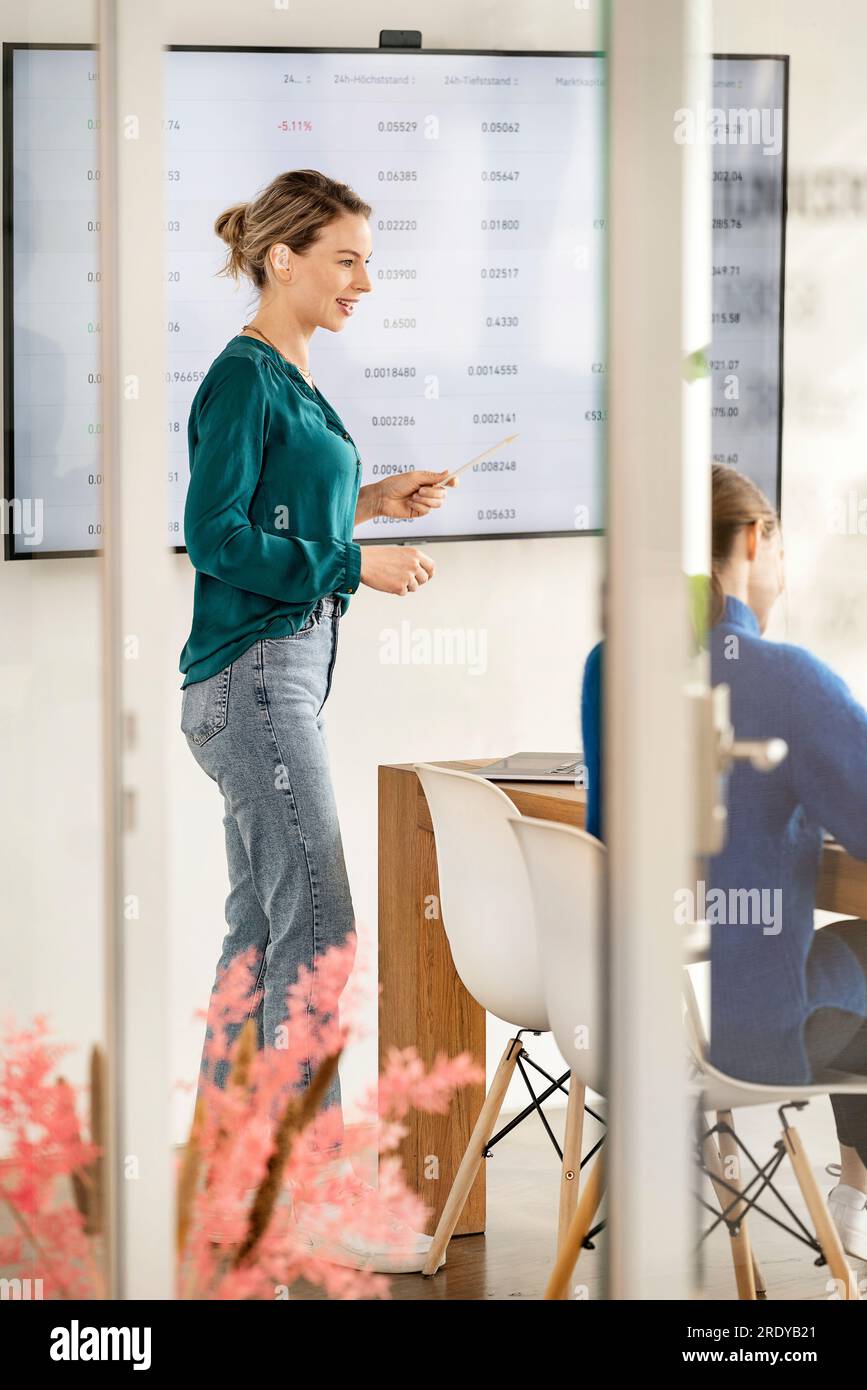Glückliche Geschäftsfrau, die im Büro vor einem interaktiven Whiteboard steht Stockfoto