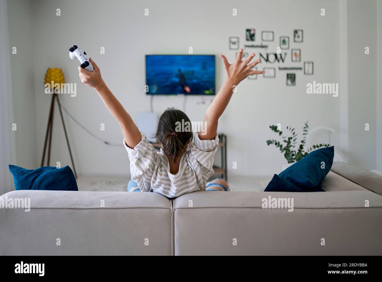 Glückliche Frau, die im Videospiel gewinnt und zu Hause mit erhobenen Armen sitzt Stockfoto