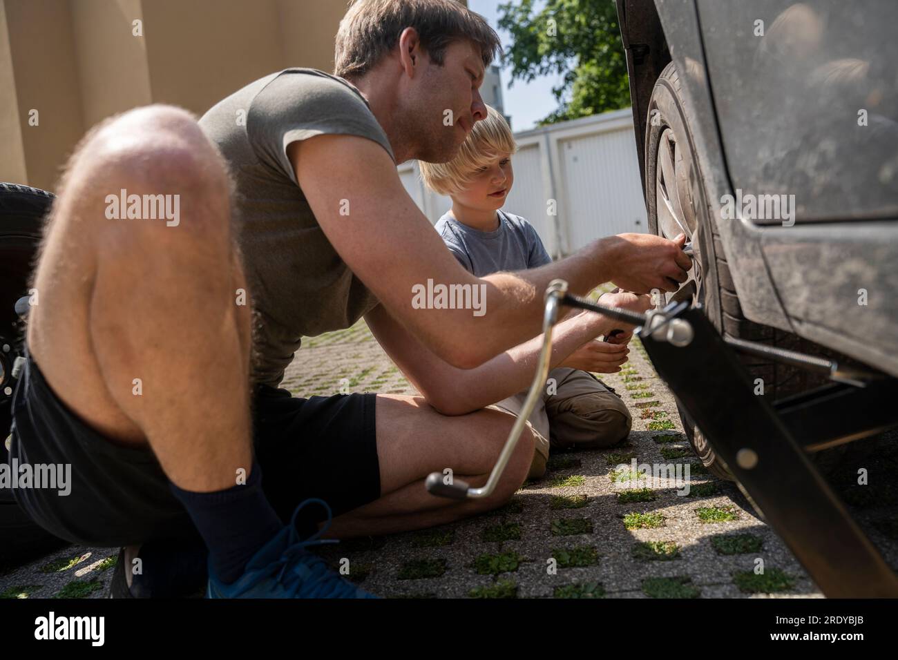 Ein Mann wechselt den Autoreifen mit dem Sohn im Hof Stockfoto