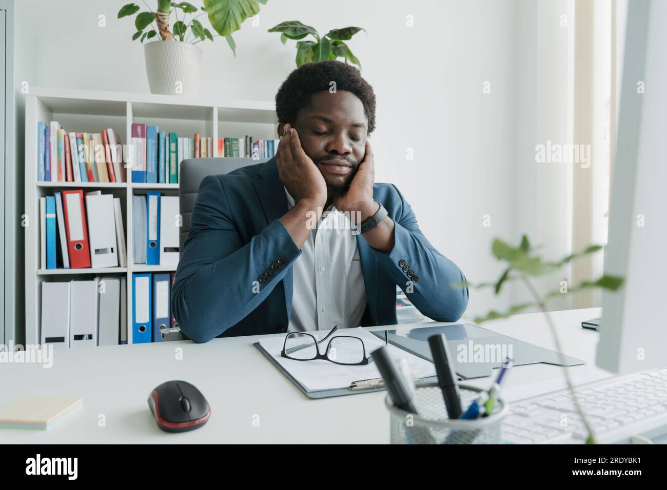 Junger Geschäftsmann, der am Schreibtisch im Büro auf Ellbogen gelehnt ist und ein Nickerchen macht Stockfoto