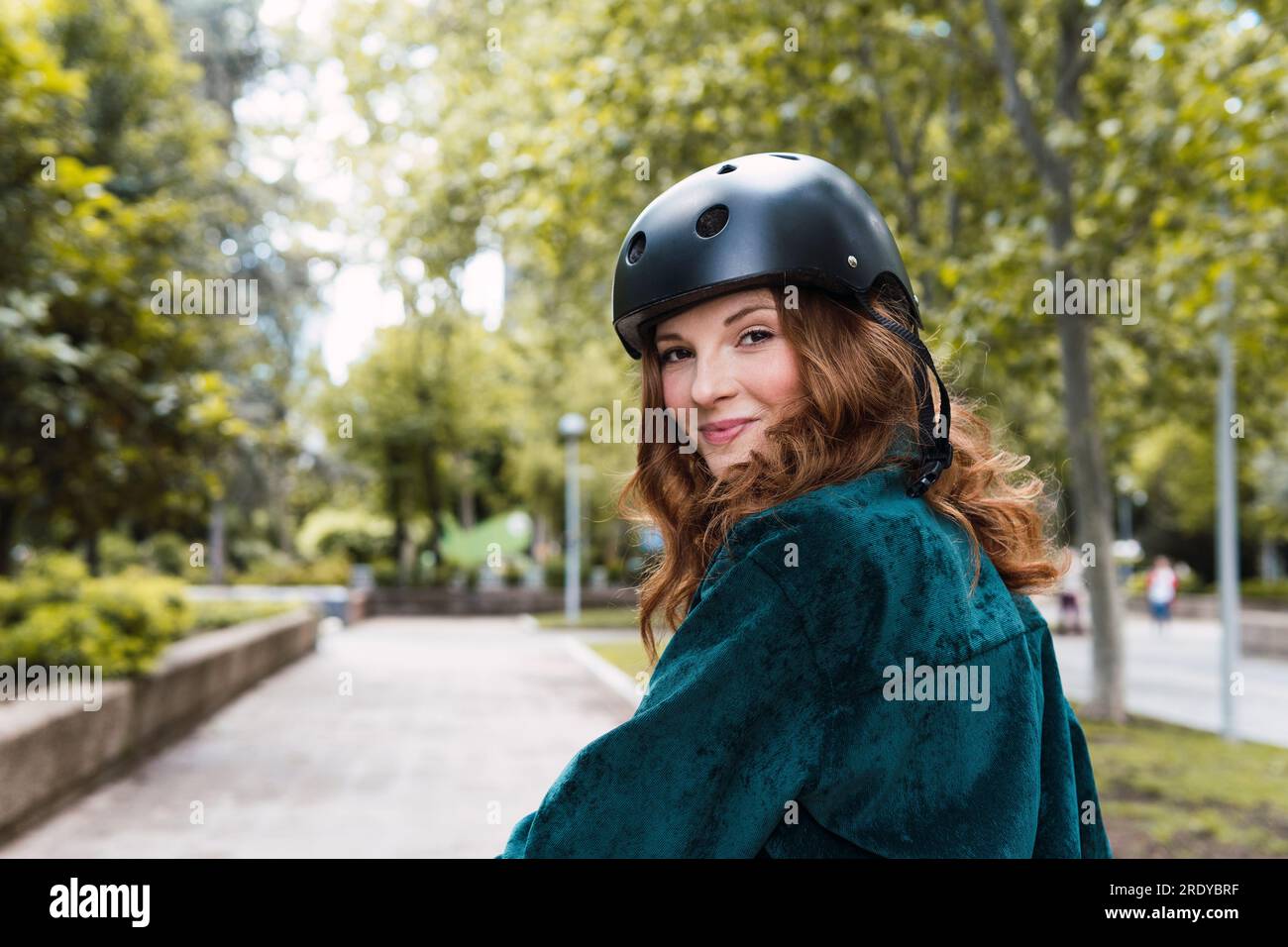 Lächelnde junge Frau mit Helm im Park Stockfoto