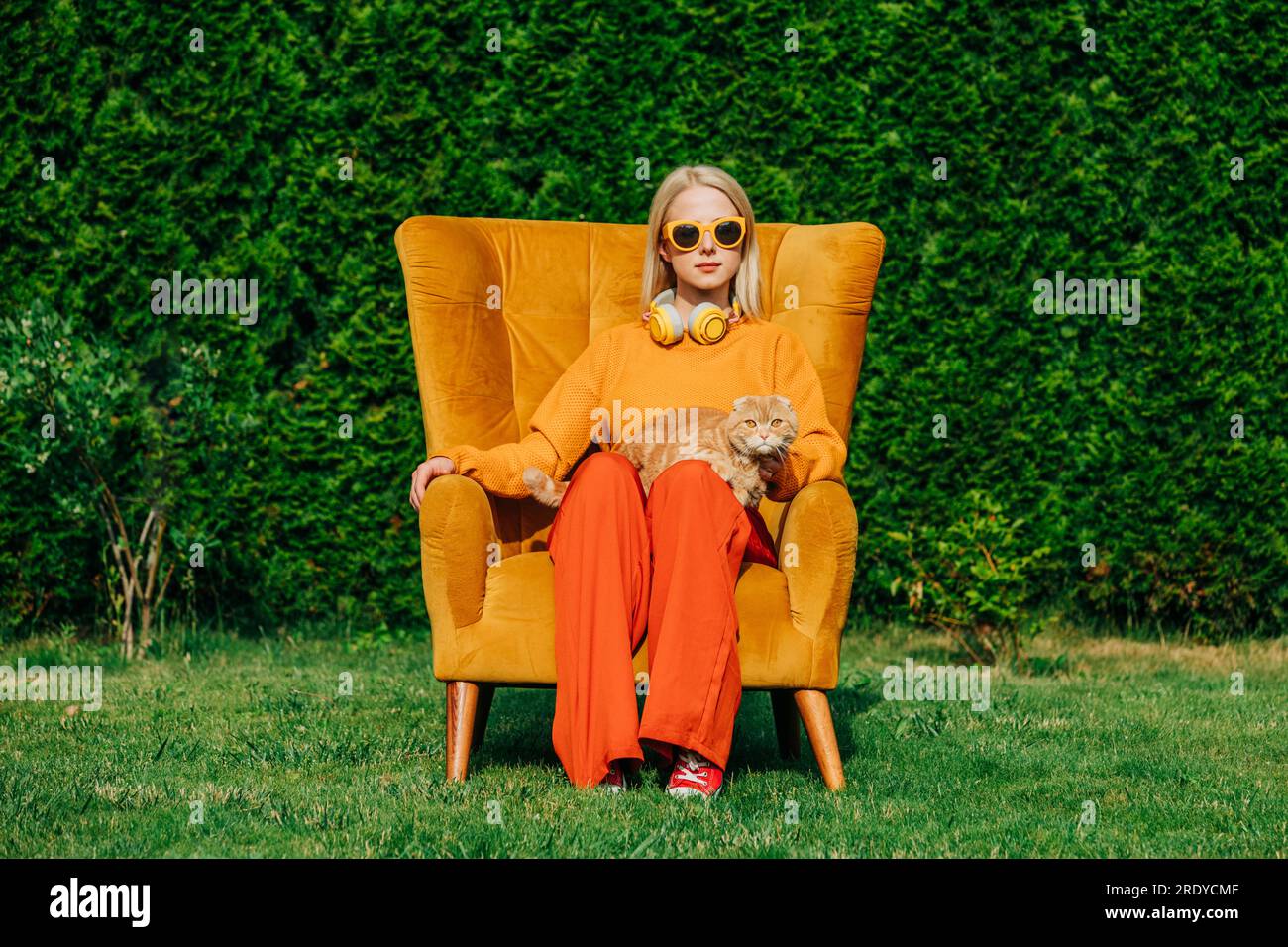 Eine blonde Frau mit Sonnenbrille, die mit der Katze auf dem Stuhl sitzt Stockfoto