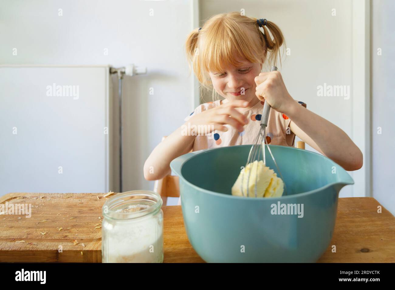 Lächelndes Mädchen, das zu Hause Kuchenteig mit Schneebesen macht Stockfoto