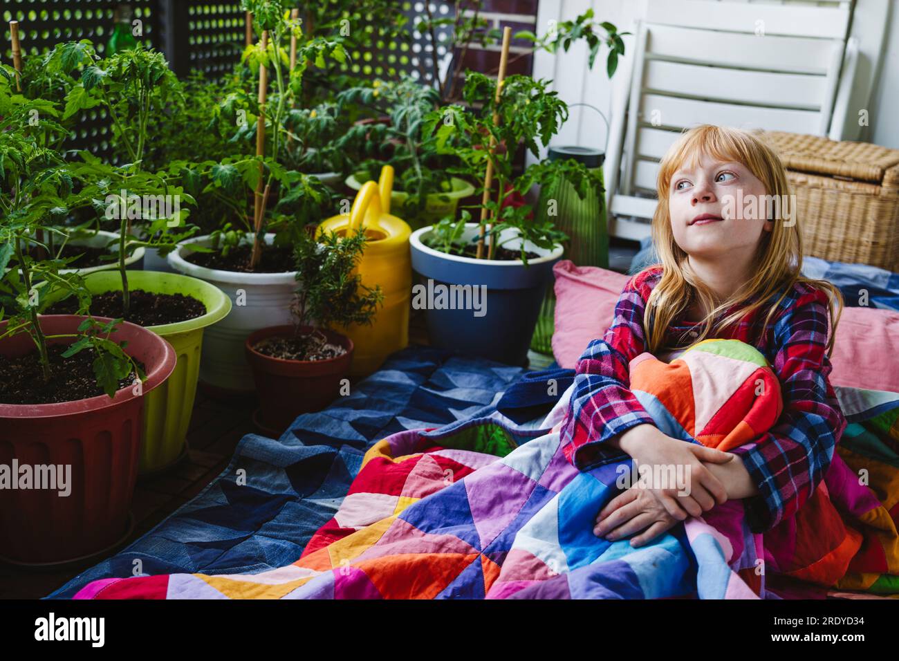 Ein aufmerksames Mädchen, das in eine Decke gewickelt ist und auf dem Balkon sitzt Stockfoto