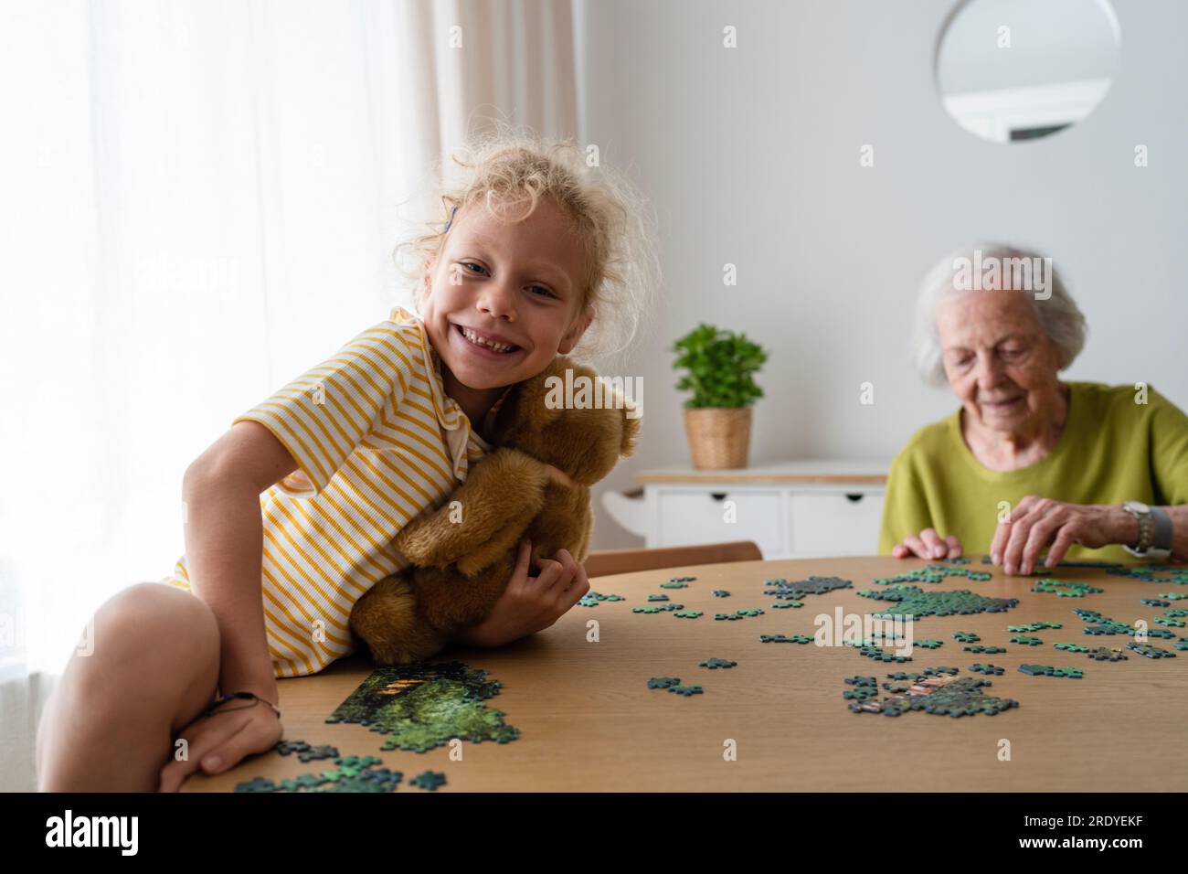 Großmutter löst Puzzle und Enkelin hält Teddybär Stockfoto