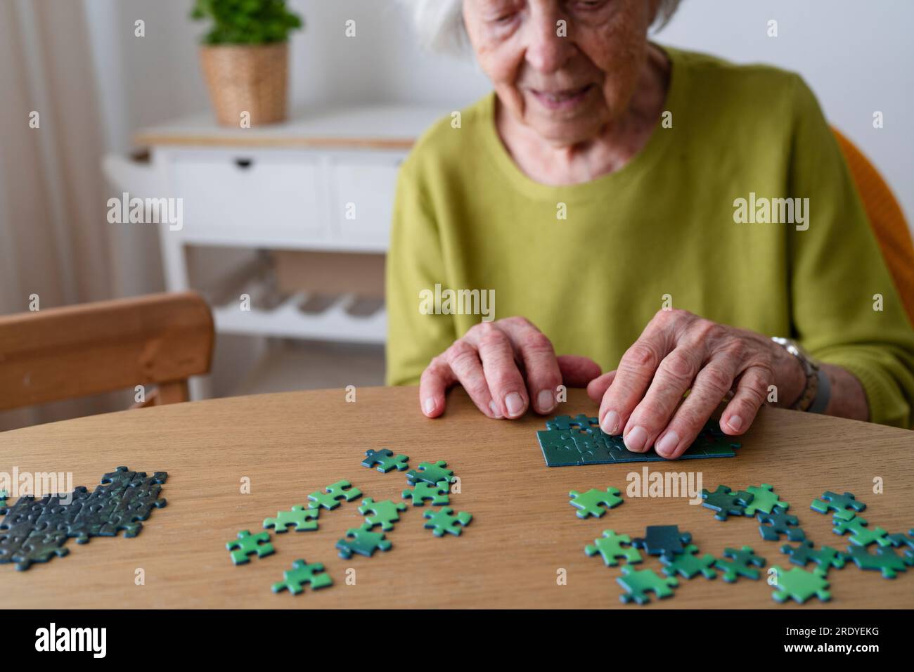 Seniorin löst Puzzle zu Hause auf dem Tisch Stockfoto