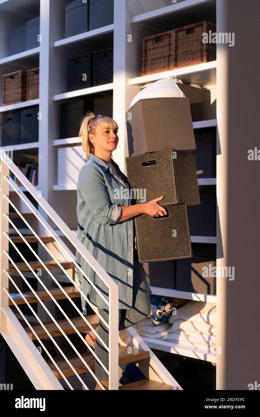 Lächelnde Frau mit Kisten, die sich zu Hause auf der Treppe bewegen Stockfoto