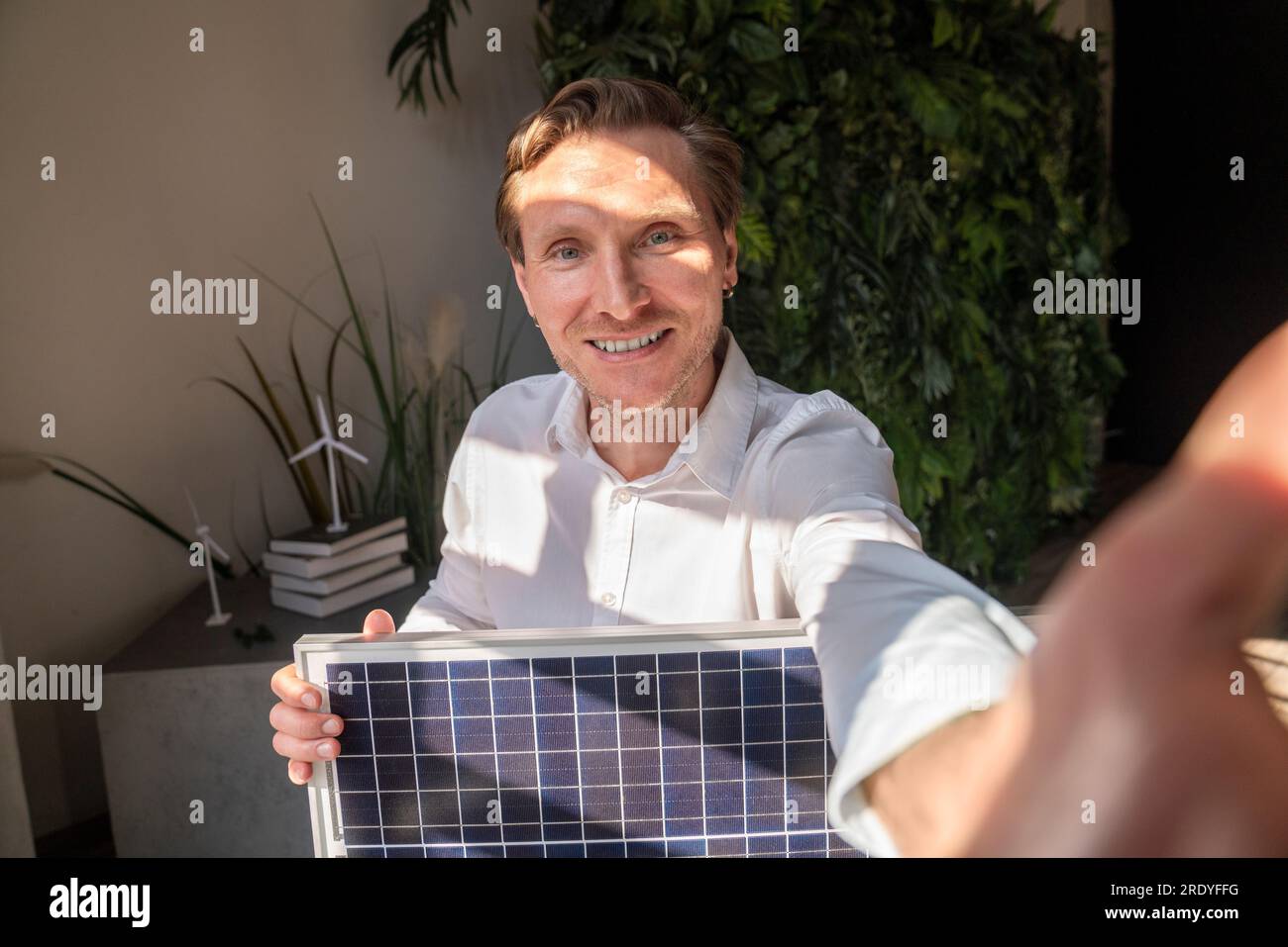 Glücklicher Geschäftsmann, der Selfie mit Solarmodul im Büro macht Stockfoto