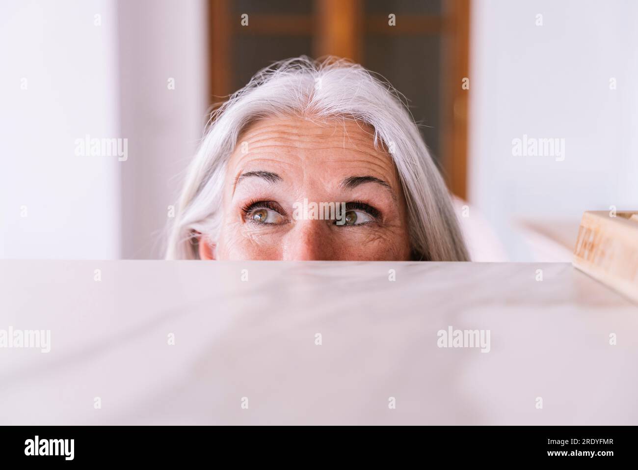 Verspielte Frau, die zu Hause hinter der Küchentheke guckt Stockfoto
