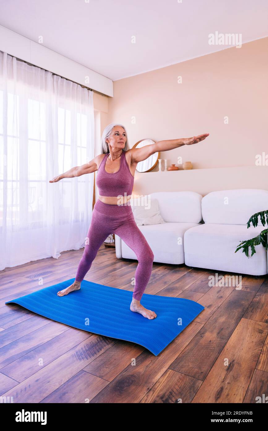Frau, die zu Hause mit ausgestreckten Armen auf Yogamatte trainiert Stockfoto
