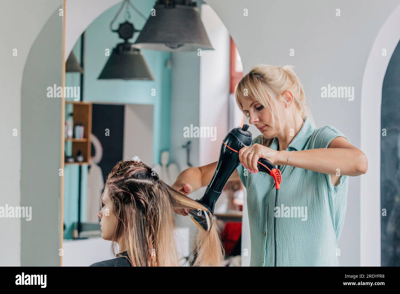 Friseur, der die Haare junger Klienten im Salon trocknet Stockfoto