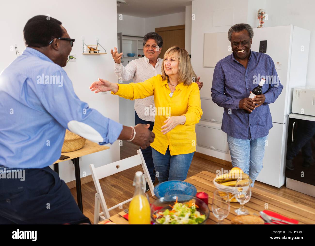 Glückliche ältere, multikulturelle Freunde kommen zu Hause zum Abendessen an Stockfoto