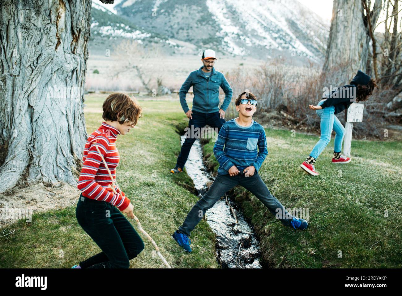 Vater und drei Kinder stehen über und in der Nähe eines Bachs Stockfoto