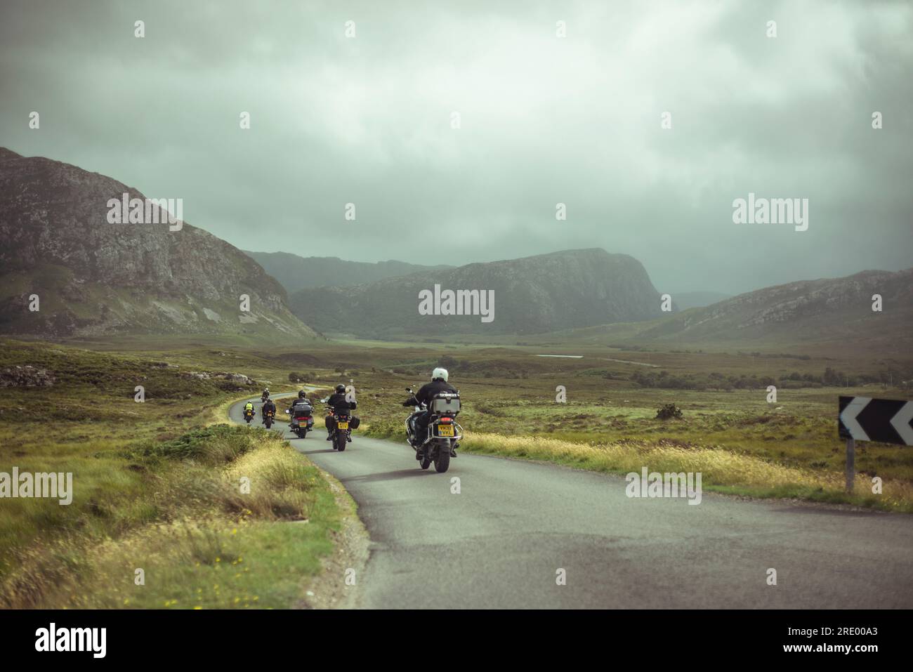 Eine Reihe von Motorrädern fährt auf einer kleinen kurvenreichen Straße durch abgelegene Berge Stockfoto