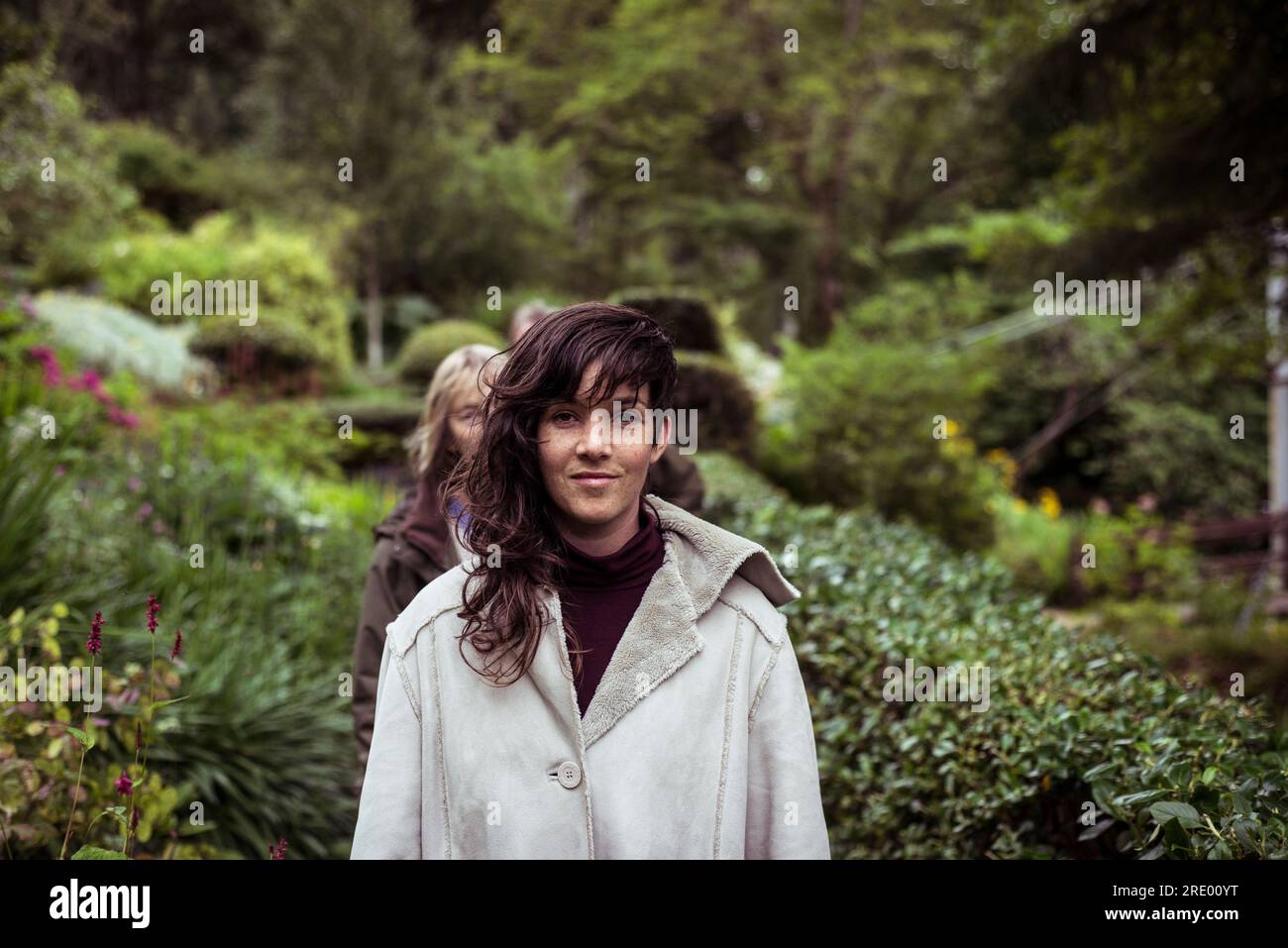 Ein Mädchen mit langen wellenförmigen Haaren und warmer Jacke läuft lächelnd durch den Garten Stockfoto