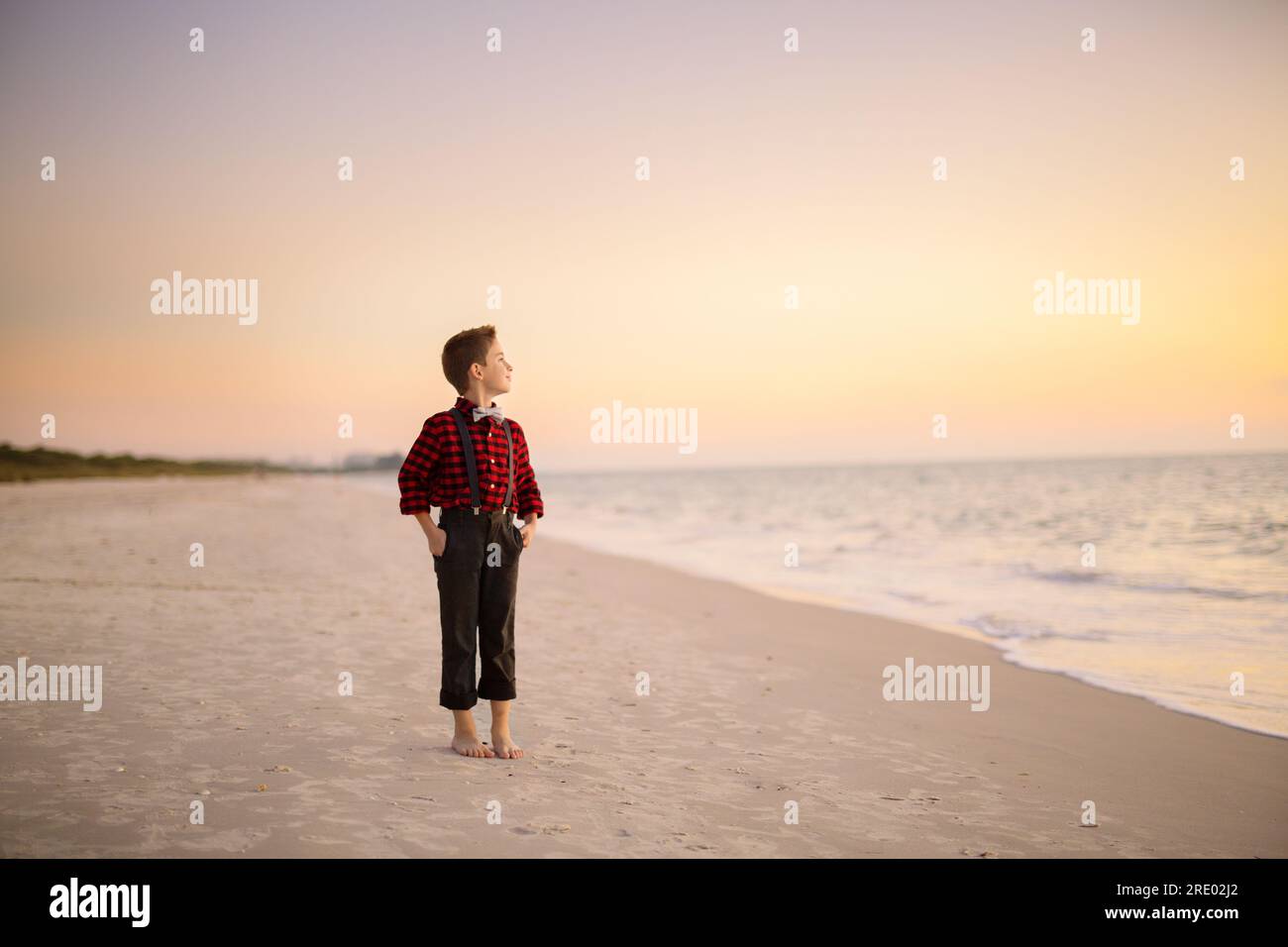 Junge Junge stand am Strand bei Sonnenuntergang Stockfoto